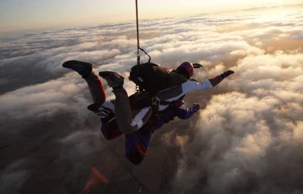 An image of tandem skydivers from above, overlooking the clouds and view of North Lincolnshire at sunset.