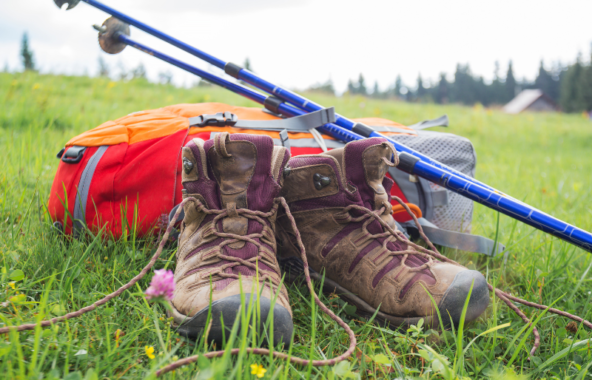 A pair of walking boots with a backpack and walking sticks resting on top in a field.
